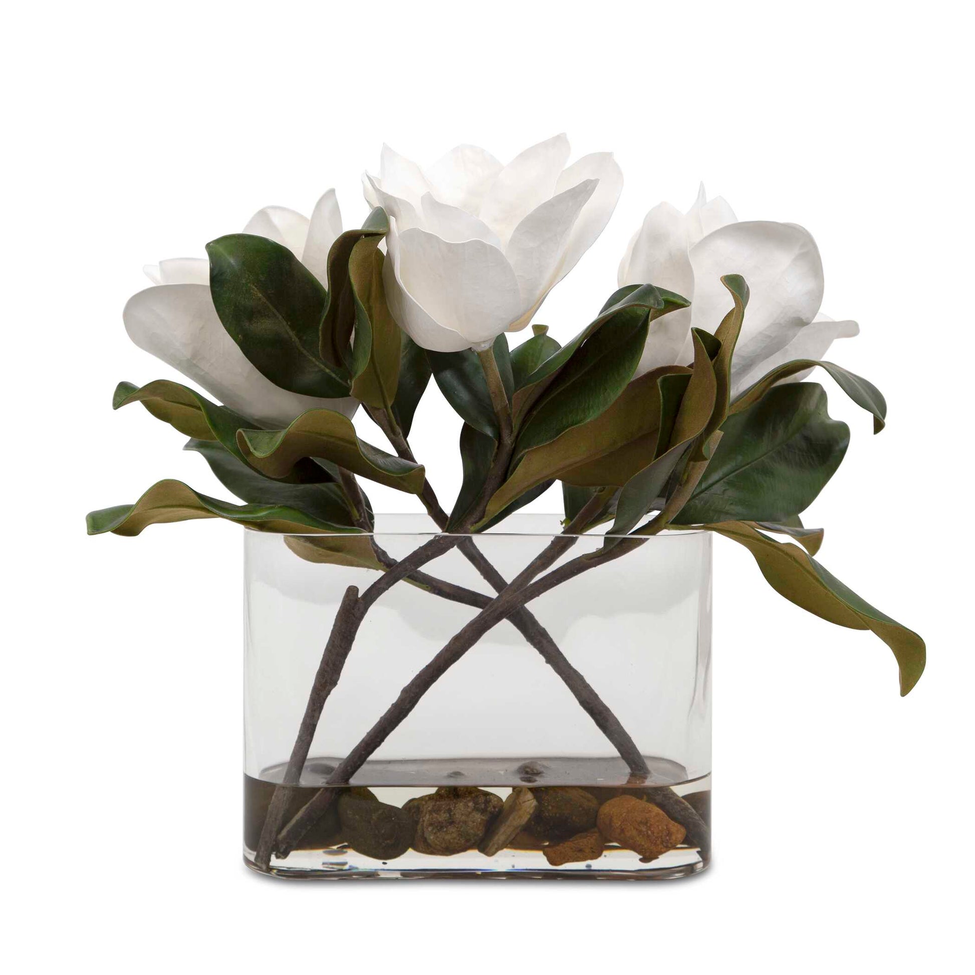 A Trio Of White Magnolia Blooms Are Placed In A Clear Glass Vase With Faux Water And Natural River Stones.